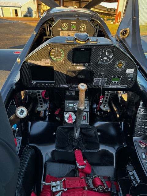 XA-42 aerobatic aircraft cockpit interior — carbon fiber panel, control stick, and red harness